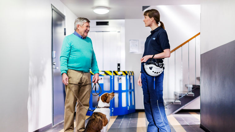 KONE Services / Elevator technician in a hallway conversing with a man with dog - KONE Modernization.